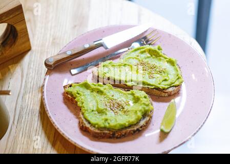 Closeup shot of two sandwiches with avocado and sesame seeds on a pink plate with cutlery Stock Photo