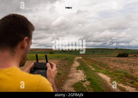 Back View Of An Unrecognizable Caucasian Young Adult Flying A Drone In A Sustainable Windmill Field. Learning Concept. Stock Photo