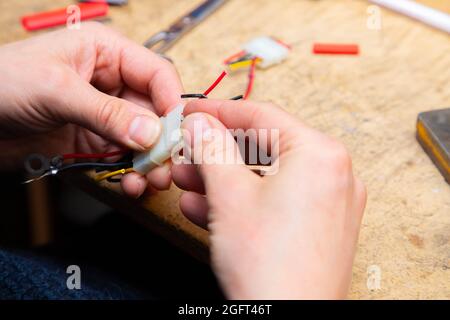 Young man's hands hold multicolored wires over desk with tools Stock Photo