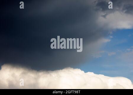 Dark grey storm clouds moving over top of white cumulus cloud on sunny day Stock Photo