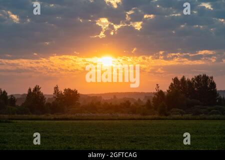 Colorful sunrise in rural with a sun shining above treetops. Lush vegetation, clouds colored red, yellow, orange. Scenic view, travel, admiring, touri Stock Photo