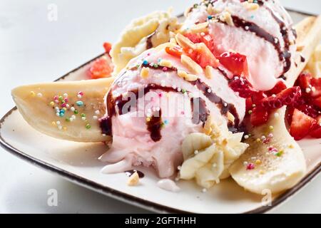 Close up on a delicious banana split with berry ice-cream, fresh strawberries, whipped cream and colorful candy pearls drizzled with chocolate served Stock Photo