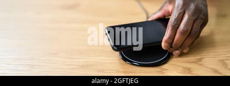 Man Charging Smartphone Using Wireless Charging Pad At Home Stock Photo