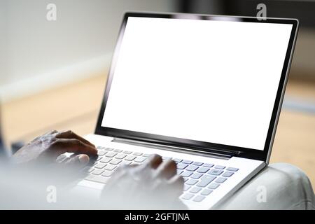 African Man On Couch Using Laptop With Empty Screen Stock Photo