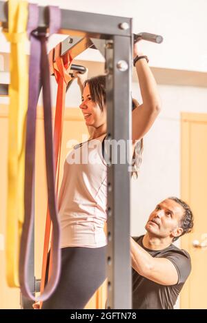View of a athlete woman doing pull ups exercise with bar with help of trainer Stock Photo