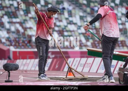 Tokio, Japan. 27th Aug, 2021. Paralympics: Athletics, long jump, in the Olympic stadium. Volunteers smoothing the sand before the competition. Credit: Marcus Brandt/dpa/Alamy Live News Stock Photo