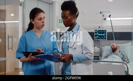 Medical nurse showing surgery expertise using tablet computer to specialist black practitioner. Hospitalized patient discussing with doctor healthcare treatment during recovery consultation Stock Photo