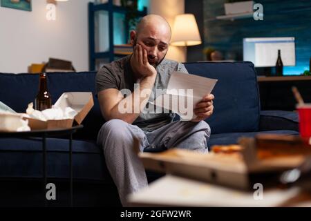 Desperate frustrated stressed young man reading letter, payment debt notification, bad financial report, eviction renter notice. Anxious, worried tenant by warning document for unpaid bank bills Stock Photo