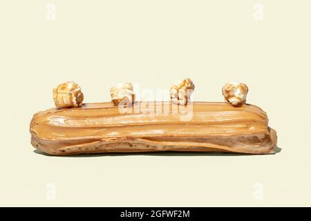 Caramel glaized eclair decorated with popcorn isolated on yellow background Stock Photo