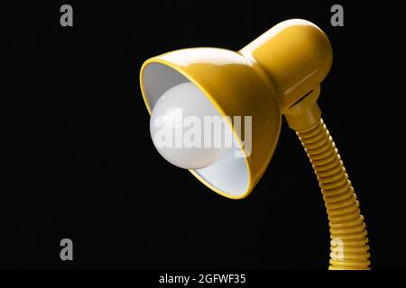 Side view of adjustable yellow desk lamp isolated on black background. Desk lamp with energy saving led light bulb. Stock Photo