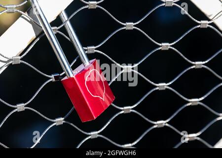 Red lock with drawing heart locked on steel net cage with dark inside. Stock Photo