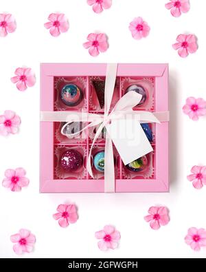 Chocolate candy. Pink gift box with handmade chocolates on white with pink flowers. Festive background. White tag. Mockup. Vertical photo Stock Photo