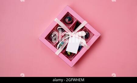 Chocolate candy. Pink gift box with handmade chocolates on a pink background. Festive background. White tag. Mockup Stock Photo