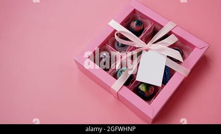 Chocolate candy. Pink gift box with handmade chocolates on a pink background. Festive background. White tag. Mockup Stock Photo