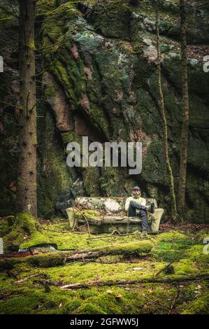 Man sitting on old sofa next to rock wall Stock Photo