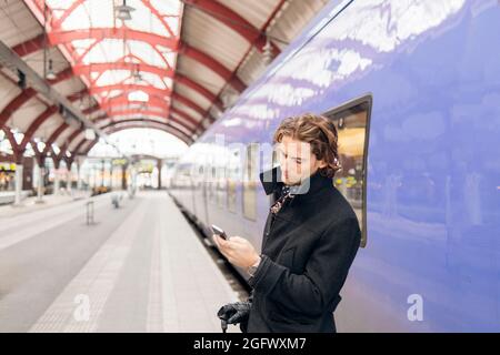 Man using phone at train station Stock Photo