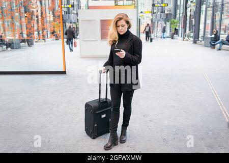 Woman with suitcase using phone Stock Photo