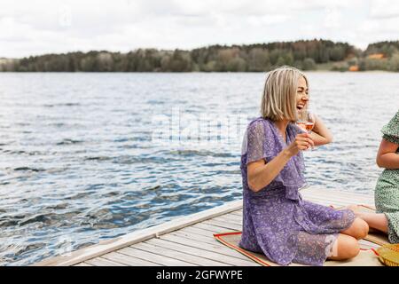 Happy woman having wine on jetty Stock Photo