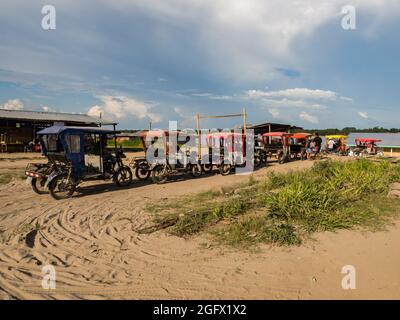Santa Rosa, Peru - December 2017: Colorful rickshaws wait for passengers on a sandy road in a small port on the Amazon River during low river water le Stock Photo