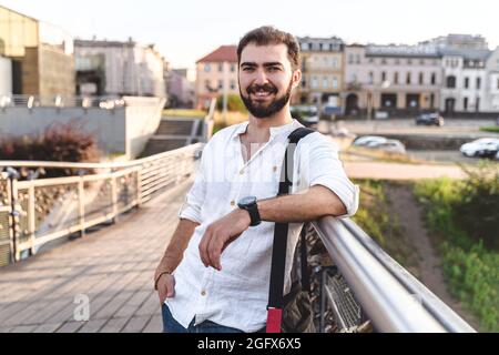 Handsome smiling man outdoors. Portrait of guy with beard in white shirt on background of city Stock Photo