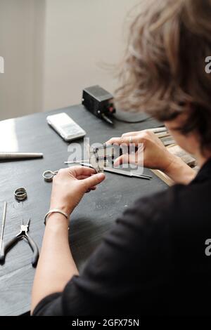Over shoulder view of female jeweler measuring ring width using caliper in workshop Stock Photo