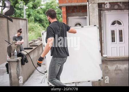 Behind the scene. Filmmaking lighting technician electric engineer adjusting reflector and setup lights diffusion intensity for movie film scene. Ligh Stock Photo