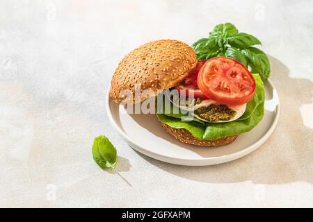 Caprese sandwich with fresh tomatoes, mozzarella cheese, pesto and basil leaves on a white plate. A healthy snack. Healthy food concept. Selective foc Stock Photo