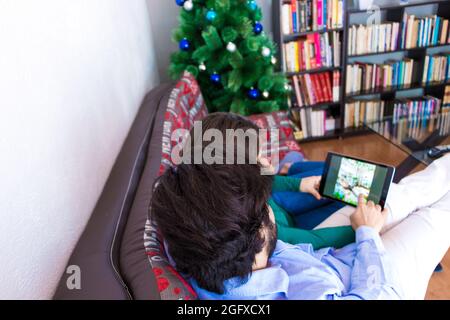 Young couple using their tablet sitting on a couch near the Christmas tree Stock Photo