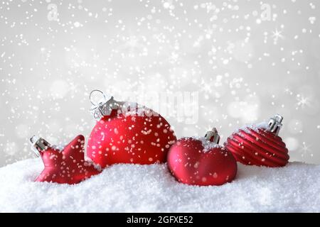 Red christmas balls, star and heart on snow while it is snowing, lots of copy or text space. Stock Photo