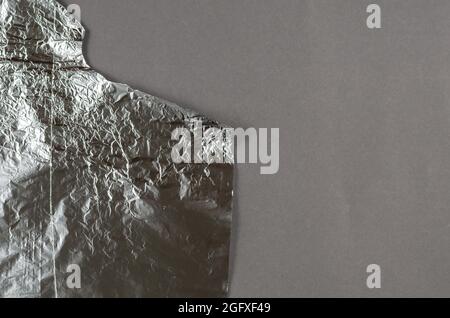 Crumpled foil against a gray background. Roll of aluminum foil for food packaging with an uneven torn edge. Food packaging. Top view. Copy space. Stock Photo