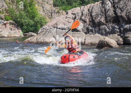 A man rowing inflatable packraft on whitewater of mountain river. Concept: summer extreme water sport,  active rest, extreme rafting. Stock Photo