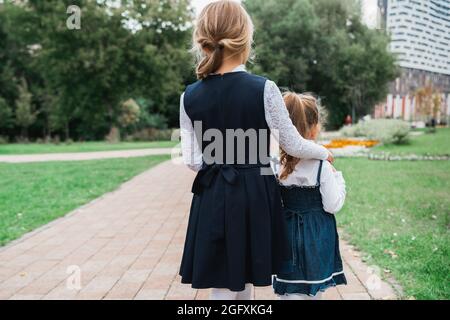 Back to elementary school concept. Little girl in school uniform goes to first grade with little sister on first of September. Ceremony of graduating. Stock Photo