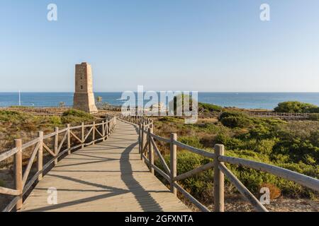 Wooden walkway at protected dune vegetation with the Moorish lookout tower, Thieves Tower, at beach Cabopino near Marbella, Andalusia, Spain. Stock Photo