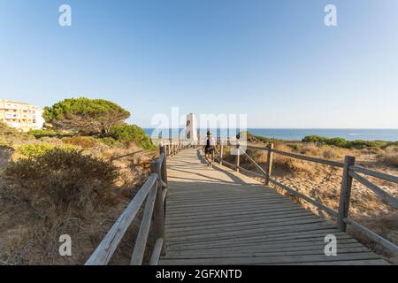 Wooden walkway at protected dune vegetation with the Moorish lookout tower, Thieves Tower, at beach Cabopino near Marbella, Andalusia, Spain. Stock Photo