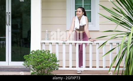 Young fitness woman in sportswear with towel standing on the balcony of the house in the morning. copy space. Stock Photo