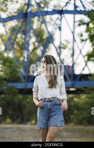 Young Spanish woman wearing shorts with a white shirt and walking in a park Stock Photo