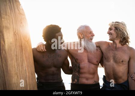 Happy fit surfers with different age and race having fun surfing together at sunset time - Extreme sport lifestyle and friendship concept Stock Photo