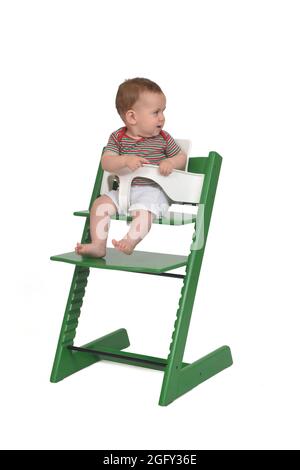 full portrait of a baby sitting looking away in a highchair on white background Stock Photo