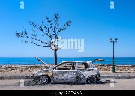A burnt out car next to the Mediterranean sea, southern Greece. Stock Photo