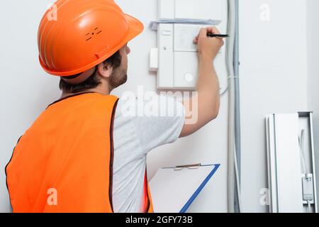 Young workman with clipboard writing on switchboard Stock Photo