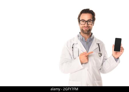 Smiling doctor pointing at smartphone isolated on white Stock Photo