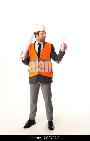 Smiling engineer with blueprint looking at model of wind turbine on white background Stock Photo