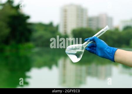 Sampling from open water. A scientist or biologist takes a sample of water from a city reservoir. A sample of water in a round chemical flask Stock Photo