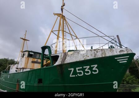 Zeebrugge Port, Belgium - August 6, 2021: Green-white and fairly rusted historic small fishing vessel Z533 out of the water on display on green lawn a Stock Photo