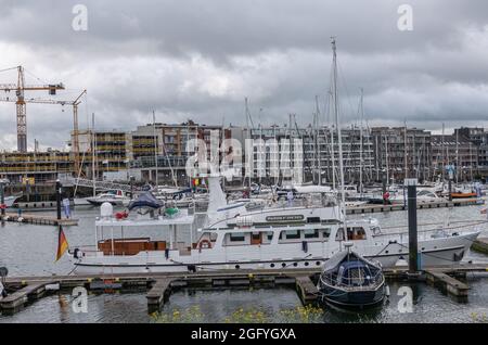 Zeebrugge Port, Belgium - August 6, 2021: Closeup of Rudolf Diesel luxury yacht docked among many smaller boats. Wall of apartment buildings in back u Stock Photo