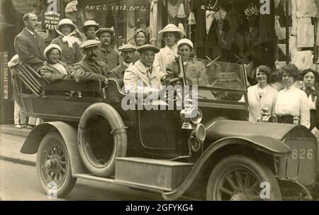 1913, a historical picture showing a group of people sitting in a motor vehicle, a Charabanc, in a street at at lIfracomble, Devon, England, UK before a sight-seeing trip  Originating in France in the 19th Century, and taken from the French word 'char a bancs' - literally, a wagon with benches - a Charabanc was an open-topped motor coach with rows of forward-facing seats. They were popular motor vehicles in Britain in the early part of the 20th century for providing large groups with day trips, excusions and works outings. Stock Photo