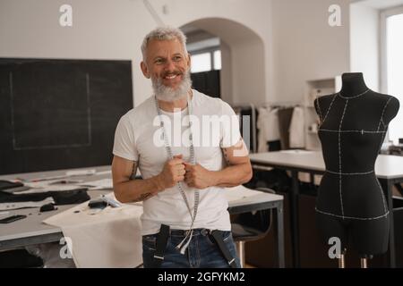 Smiling mature designer holding tape measure near mannequin Stock Photo