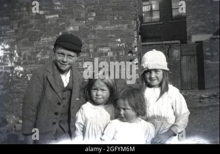 1920s, historical, a young boy wearing a wool suit and hat, with his three little sisters, standing together outside in a victorian back-street, for a photo, England, UK. Stock Photo