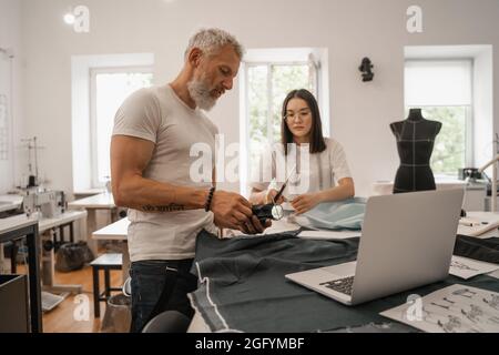 Designer holding color swatches near laptop and blurred asian colleague Stock Photo
