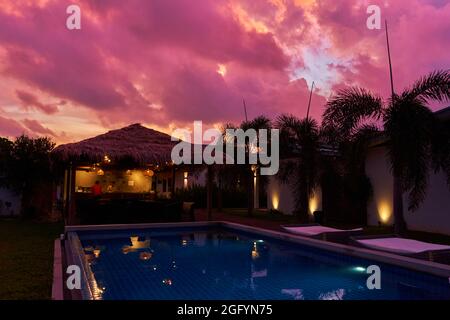 A gentle sunset sky over a thatched bungalow. An exotic resort in the tropics. Stock Photo